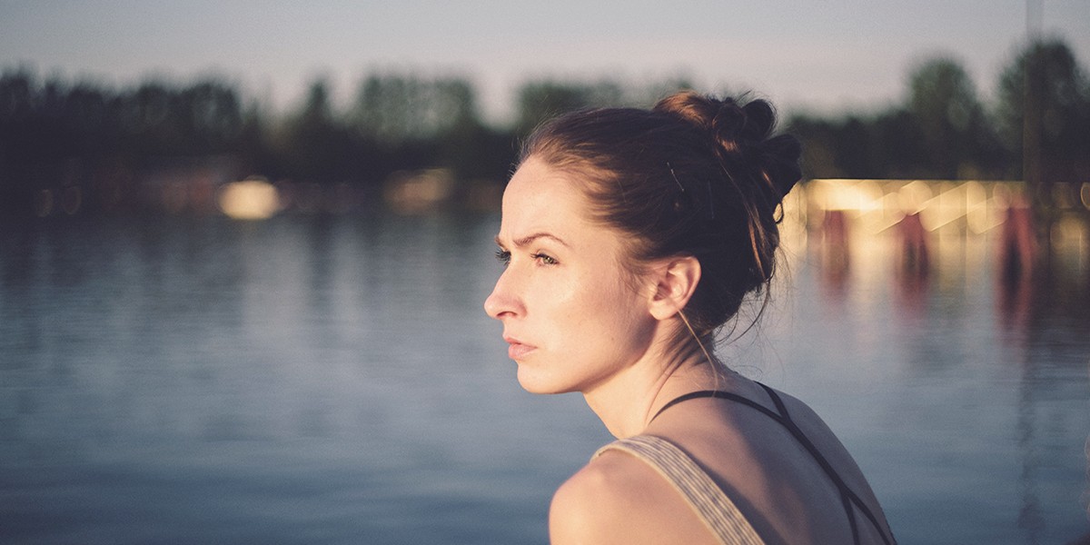 μια νεα γυναίκα καστανή μπροστά σε μια λίμνη στέκεται σκεφτηκή.